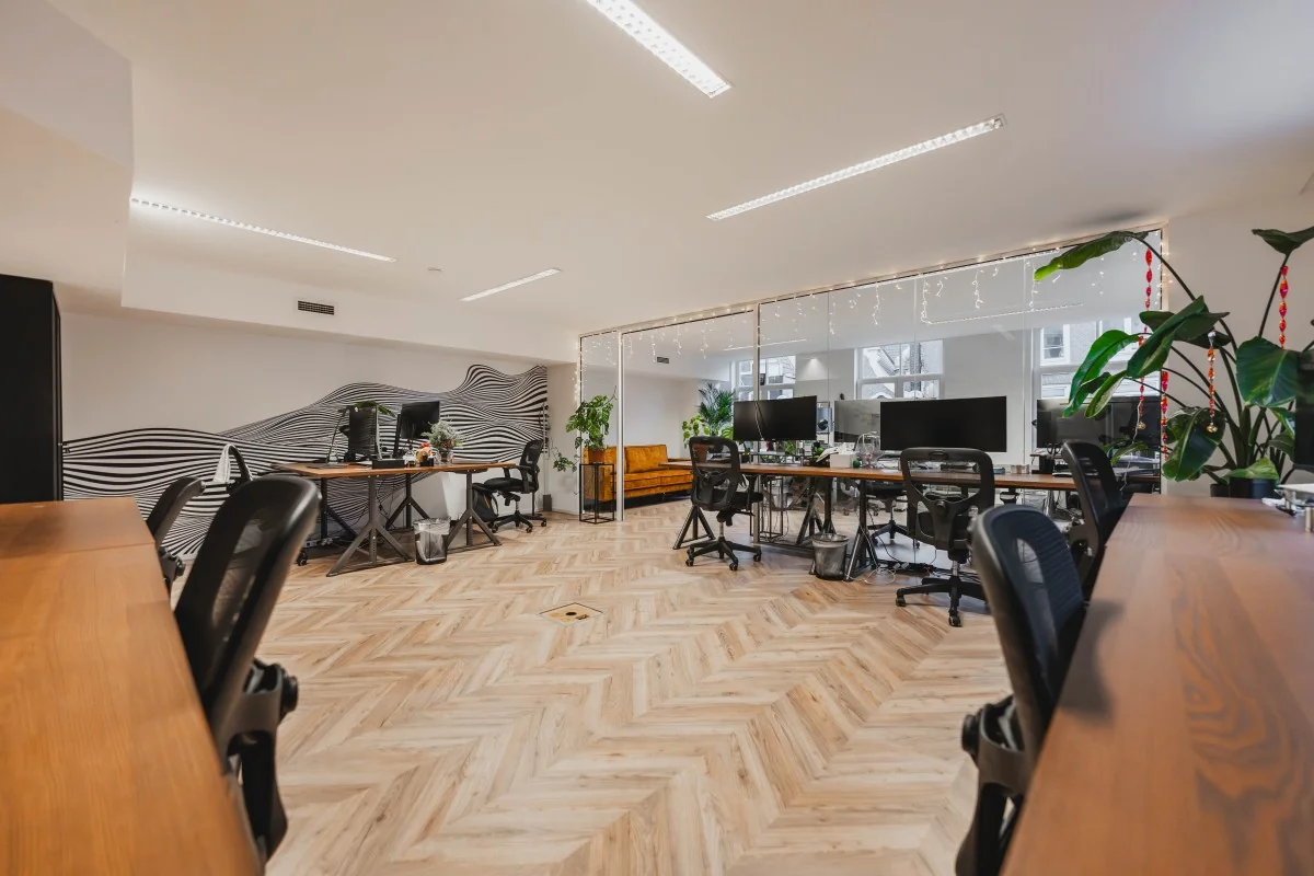 Modern kantoorinterieur aan de Korte Reguliersdwarsstraat met houten visgraatvloer, bureaus, planten en grote beeldschermen.